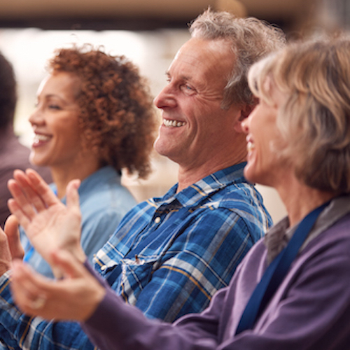 3 parents smiling and clapping during a presentation