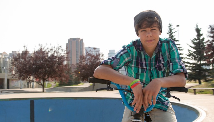 Teenage boy leaning on handlebars of bike wearing green shirt