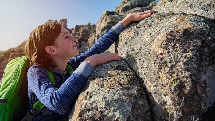 teenage girl climbing a boulder with backpack on