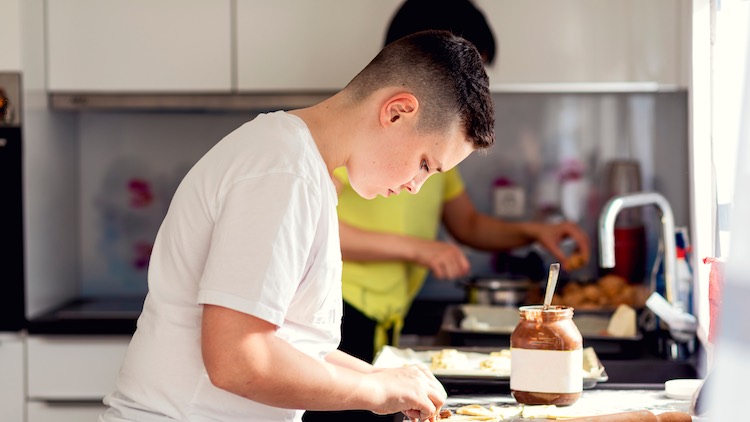 teen boy in white shirt at kitchen bench creating pastry 