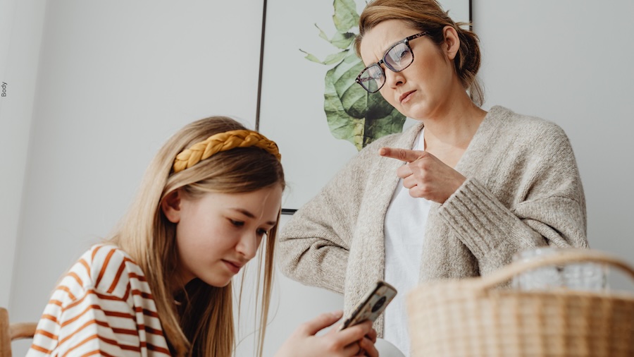 Mother pointing at daughter who is staring at a mobile phone