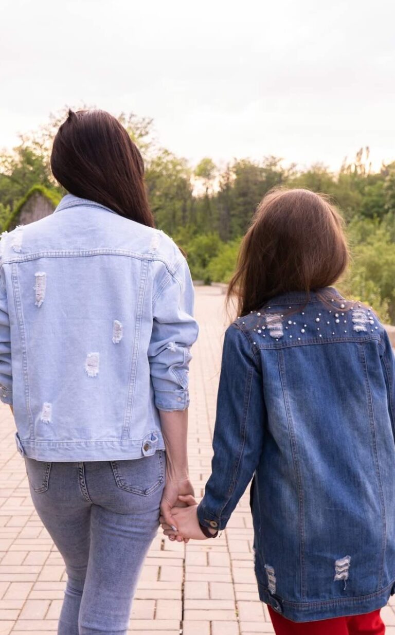 Mother and teenage daughter holding hands while walking outdoors, symbolising connection and support in parenting teenagers.